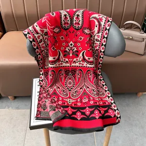 Gros plan d'un châle rouge à motif cachemire avec détails de glands noirs sur une chaise