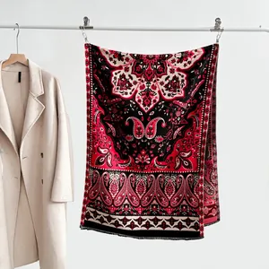 Détail des motifs cachemire et des franges à glands sur un châle rouge et noir élégant