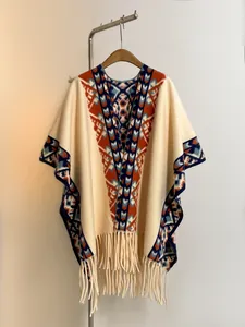 Détail d'un poncho en tricot à motifs tribaux avec ourlet à franges sur un cintre en bois