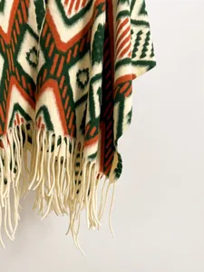 Detail of bohemian knit shawl with forest green geometric patterns and thick cream tassels