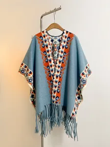 Détail du poncho en tricot bleu clair avec motifs géométriques orange et franges