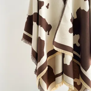 Detailed close-up of cow print shawl fabric with soft fringe and thick knit texture
