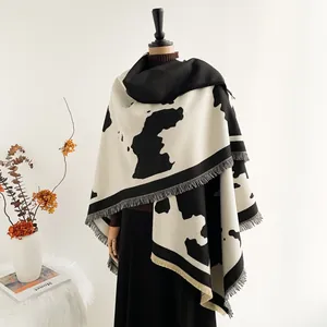 Thick travel shawl featuring black and white cow print texture and fringe tassels