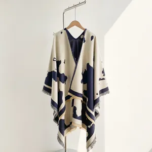 Detail of knit travel poncho with blue cow print and tassel fringe on beige fabric