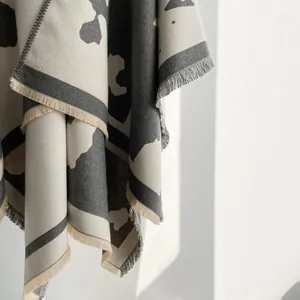 Detail of grey and beige thick scarf with abstract patterns and fine fringe trim