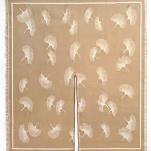 Detail of knit shawl featuring white ginkgo leaf patterns and fringe on caramel fabric