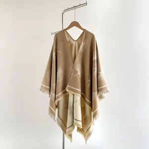 Close-up of beige knit poncho featuring white ginkgo leaf jacquard and fringe hem