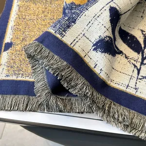 Detail of woven floral tapestry with navy blue and gold leaves and fringe edges