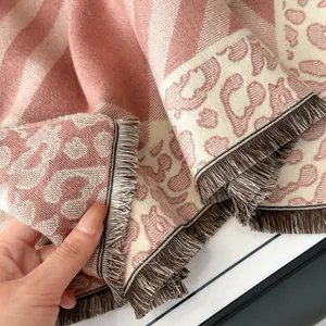 Close-up of thick knit scarf with leopard pattern, striped texture and coffee tassels