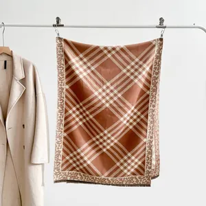 Detail of plaid scarf with leopard print borders and fringes on a minimalist hanger