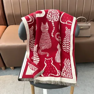 Red cashmere-like scarf with cat jacquard patterns and tassels draped on a leather chair