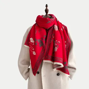 Dettaglio dello scialle rosso con ricami floreali e nappe su cappotto beige