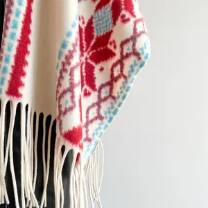 Detailaufnahme von Ethno-Strickschal mit roten Schneeflockenmustern und weißen Fransen