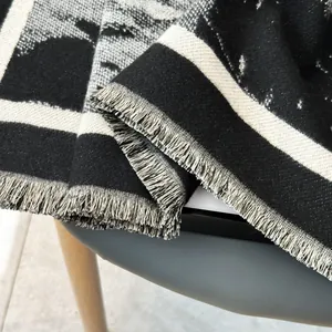 Close-up of geometric knit scarf with fringe detail in grey, white, and black tones