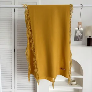 Détail d'une écharpe jaune moutarde aspect cachemire avec franges et étiquette rose