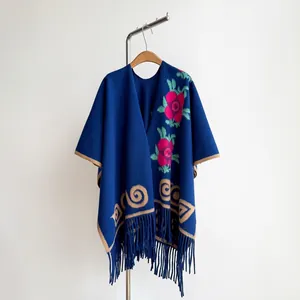 Détail d'un châle en maille bleu marine avec broderie florale rouge et franges