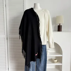 Détail d'un châle noir imitation cachemire avec franges et étiquette rose sur tricot