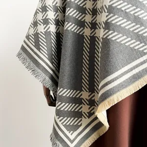 Detailed view of grey and white houndstooth pattern and soft fringe on the poncho