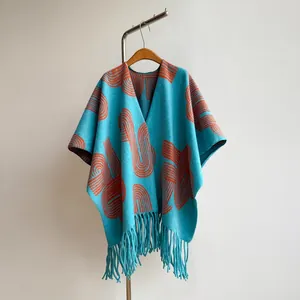 Detail of turquoise knit shawl with orange abstract patterns and fringe tassels