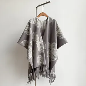 Detail of grey knitted poncho shawl with white geometric patterns and thick tassel hem