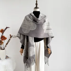 Detail view of a gray knitted shawl with white geometric patterns and long tassel edges