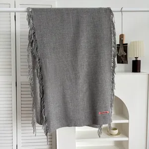 Détail de l'écharpe gris foncé avec franges à pompons et étiquette de marque tissée sur fond blanc