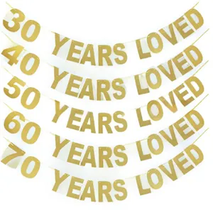 Detalle de carteles dorados con purpurina 'YEARS LOVED' para decoración de cumpleaños 30-70