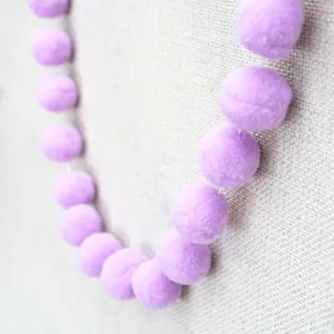 Detail view of handmade lilac fuzzy felt balls on white string for DIY party decoration