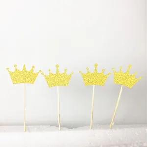Detail of four golden glitter crown cake toppers with wooden sticks on a white base