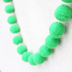 Detail of emerald green pom-pom garland with soft fiber texture for DIY party decoration