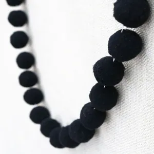 Close-up of soft black plush pom pom garland with elastic fiber texture for DIY party decor
