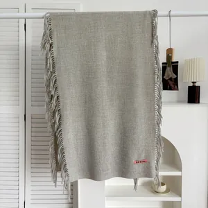 Détail d'une écharpe gris clair à franges sur un cintre blanc dans une pièce chaleureuse