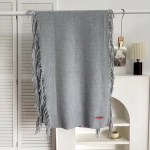 Écharpe grise aspect cachemire avec franges et étiquette tissée sur un cintre
