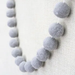 Macro shot of minimalist grey felt pompoms on a white string for party decoration