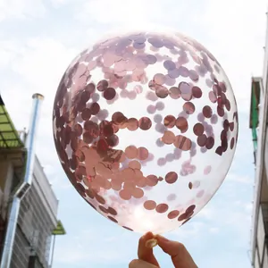 Close-up of clear balloon filled with rose gold confetti against a blue sky background