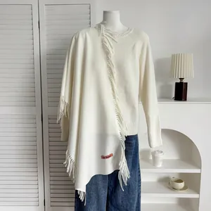 Détail du châle crème à franges avec étiquette rose sur un tissu en maille douce