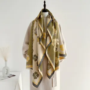 Détail d'un châle en cachemire à motif camélia avec franges olive sur un manteau beige
