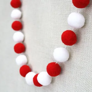 Detail of red and white wool felt pom poms on a string for birthday party decoration