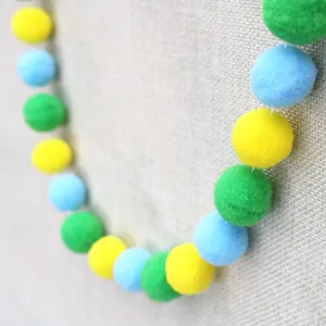 Close-up of colorful yellow, blue and green pom-poms on a rustic textured fabric