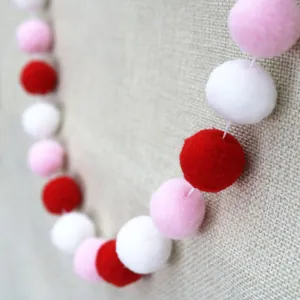 Detail of red, pink, and white plush pom-pom garland on a natural linen background