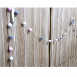 Detail of pink and grey felt ball garland hanging on wooden furniture for party decor