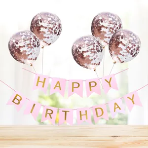 Rose gold confetti balloons and pink Happy Birthday banner set on a wooden table