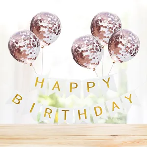 Detail of Happy Birthday gold foil banner and rose gold confetti balloons on a table