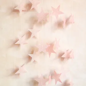 Détail d'une guirlande d'étoiles roses pailletées suspendue sur un mur texturé