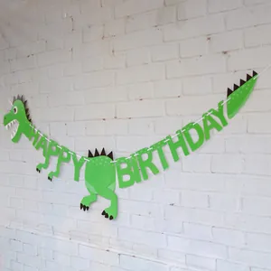 Macro shot of green dinosaur-themed Happy Birthday paper banner on white brick wall background
