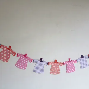 Detail of baby first birthday banner featuring numbered colorful paper clothes on white wall