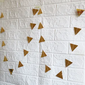 Close-up of shiny gold triangular bunting banner hanging on a white brick wall for parties