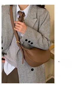 Minimalist brown pebbled leather half-moon crossbody bag shown on a model in a suit