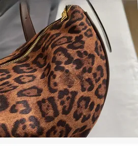 Close-up of leopard print velvet fabric with brown leather handle and gold zipper detail