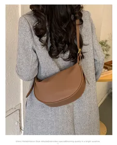 Brown leather crescent crossbody bag shown on model with grey coat from side view